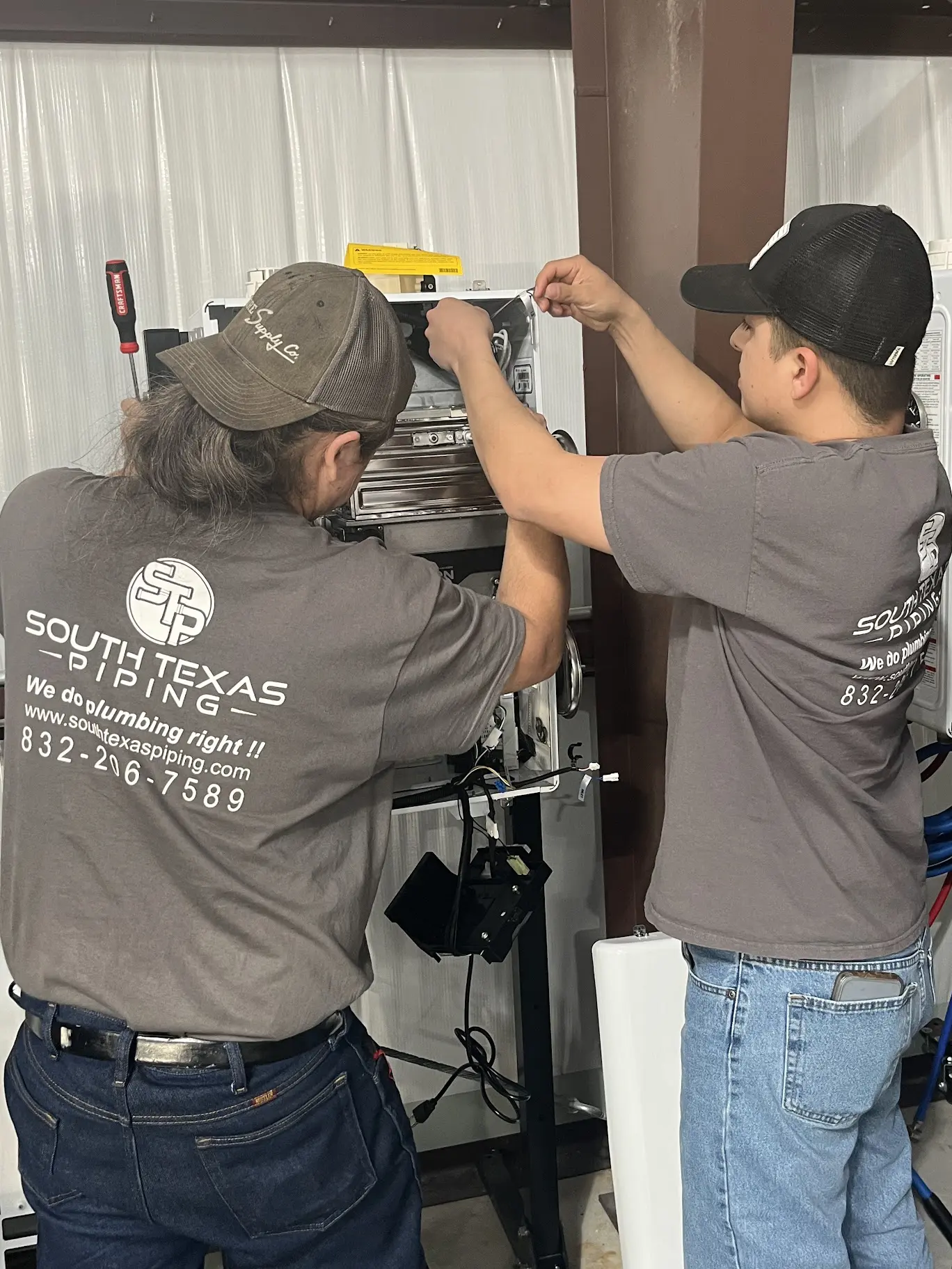 Two technicians installing or adjusting equipment on a wall.