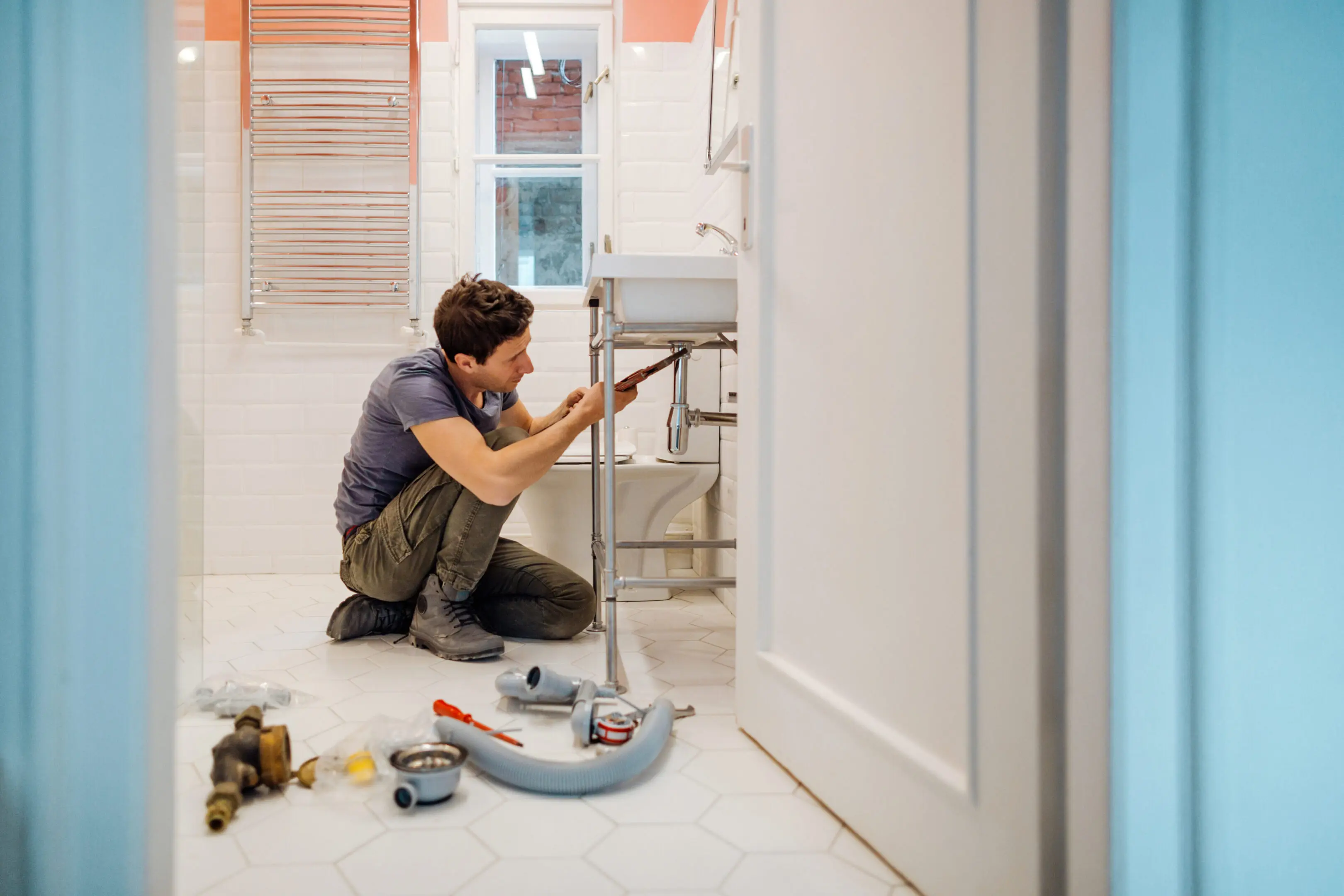 A plumber fixing a bathroom sink with tools scattered around.