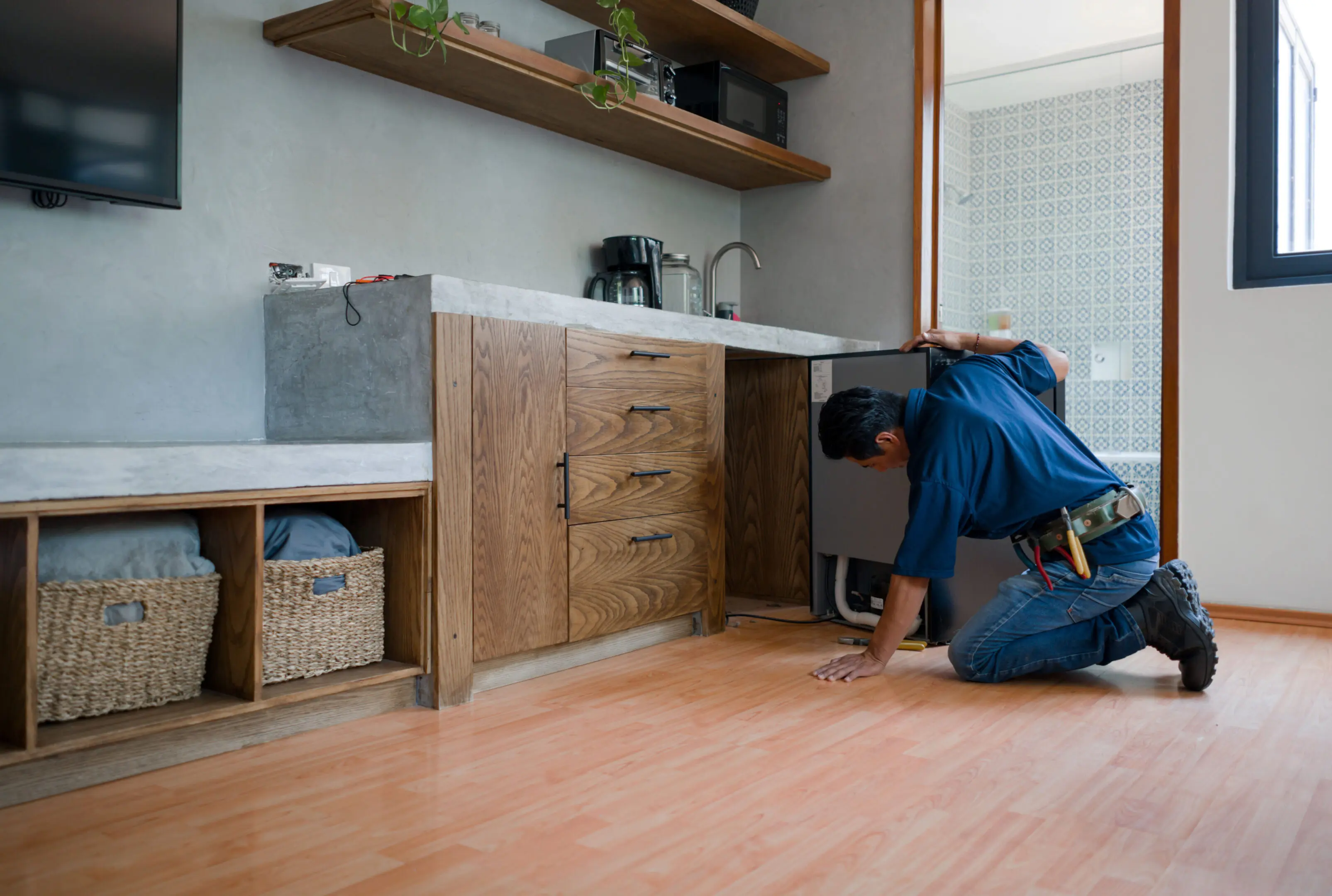 A person fixing a dishwasher in a modern kitchen.