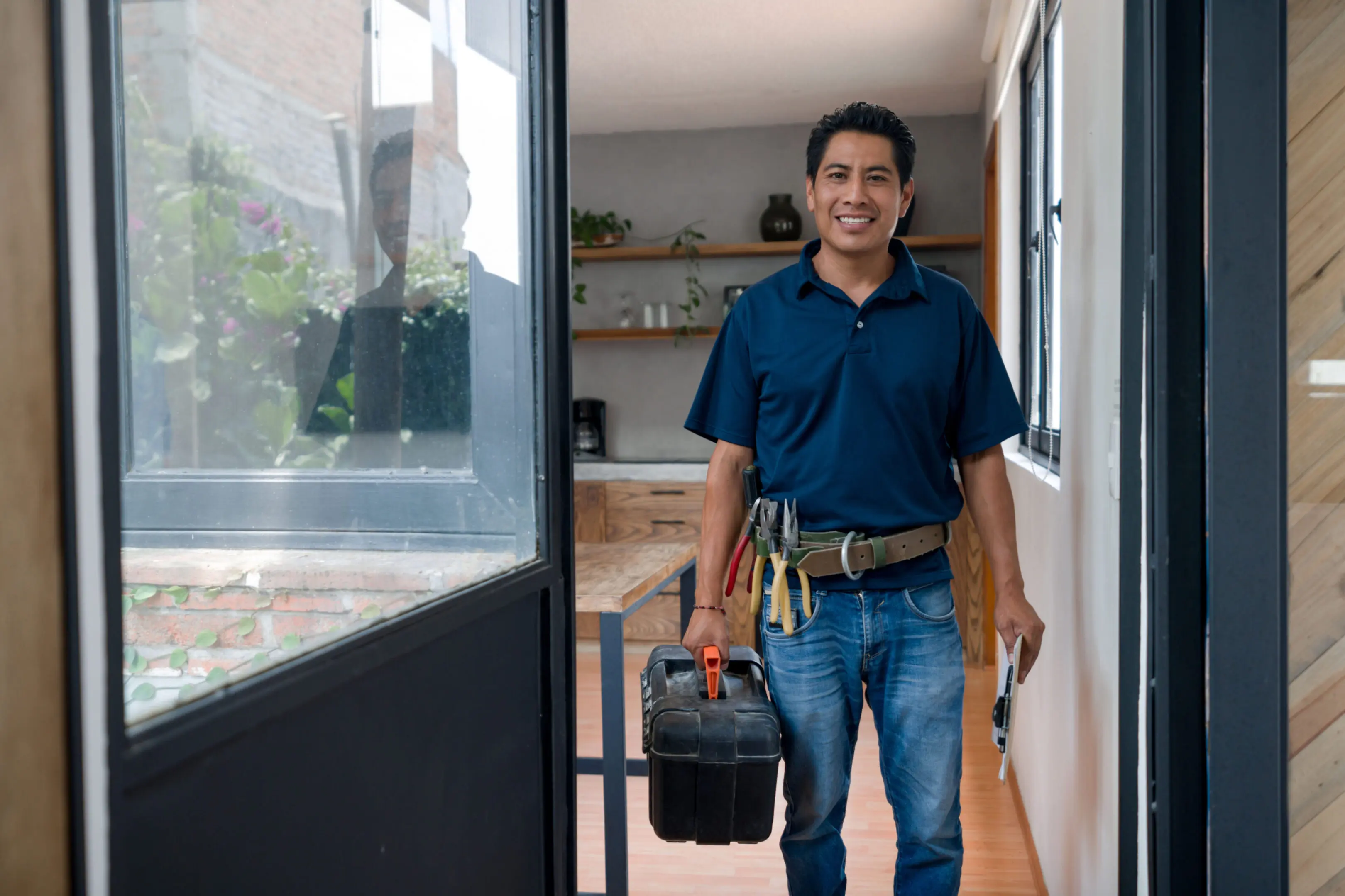 Handyman standing in a hallway with tools and a toolbox, smiling.