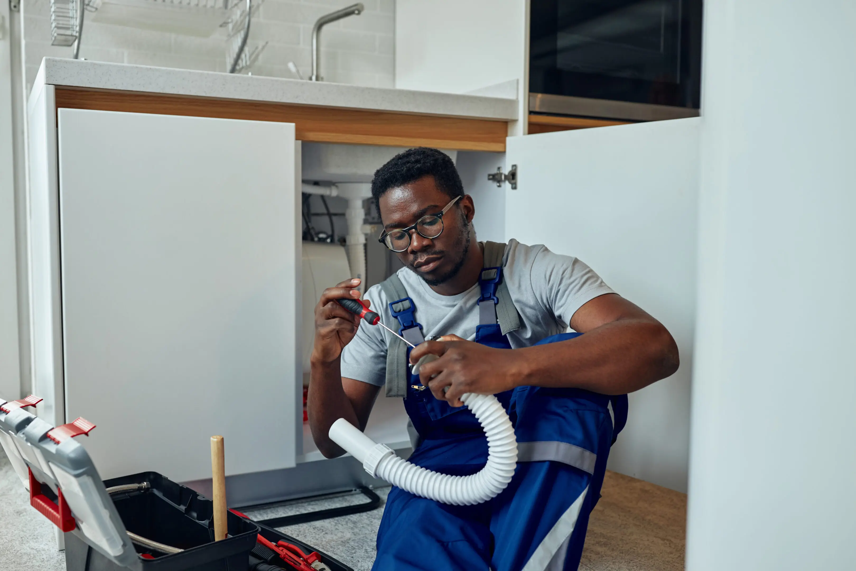 A plumber fixing a pipe under a kitchen sink.
