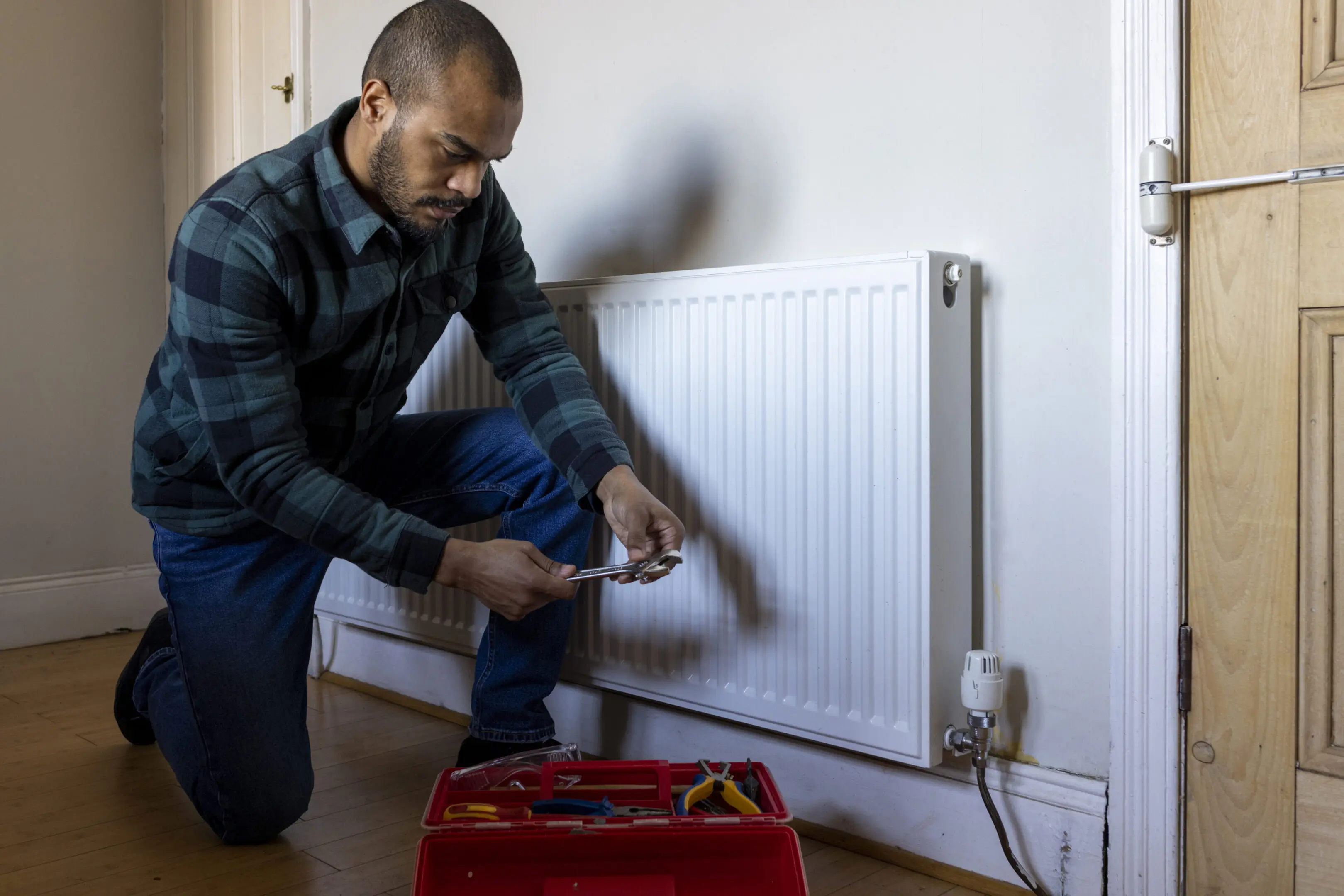 Man fixing a radiator with a wrench and toolbox.