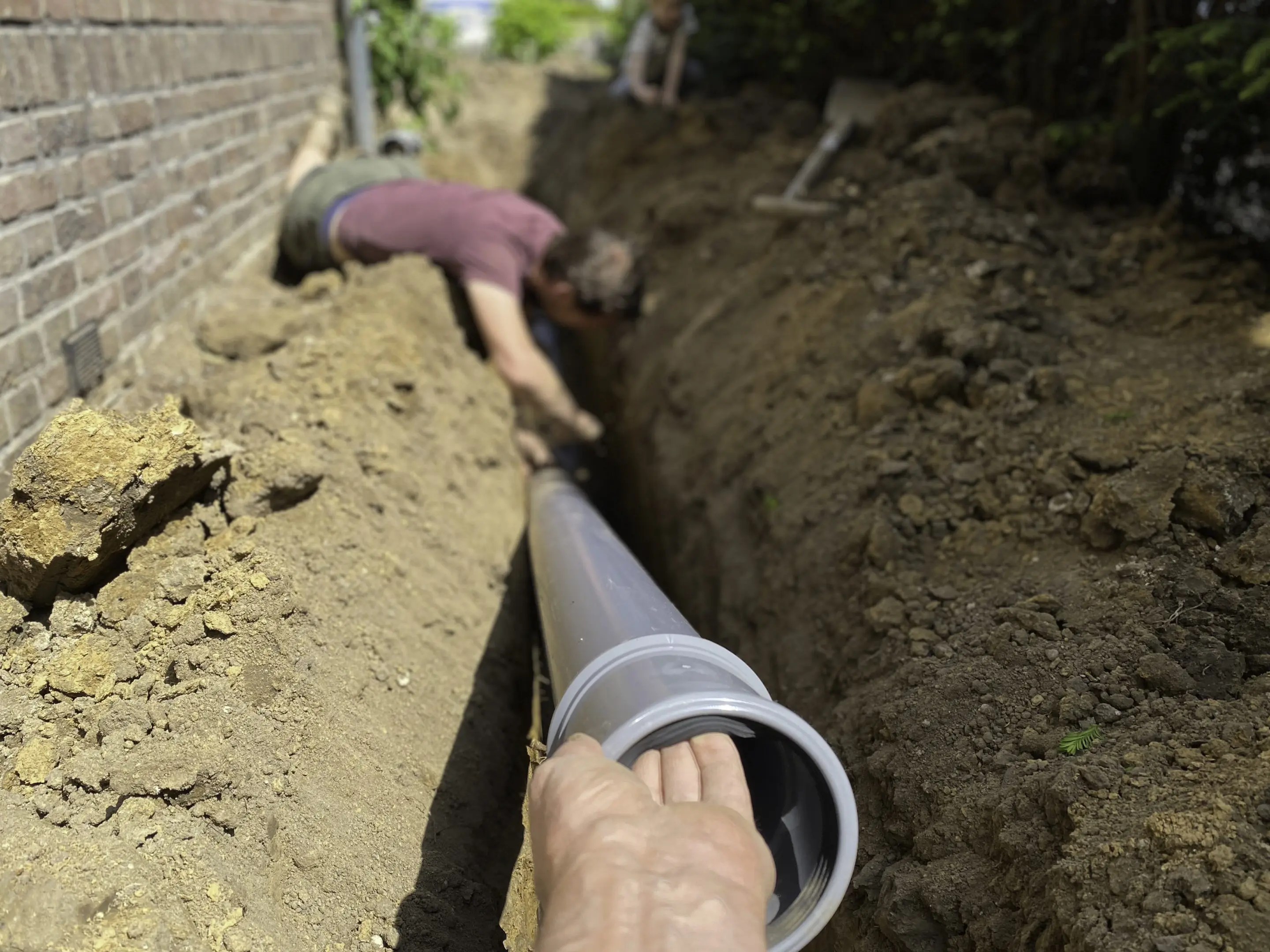 Two people installing a large pipe in a trench outdoors.