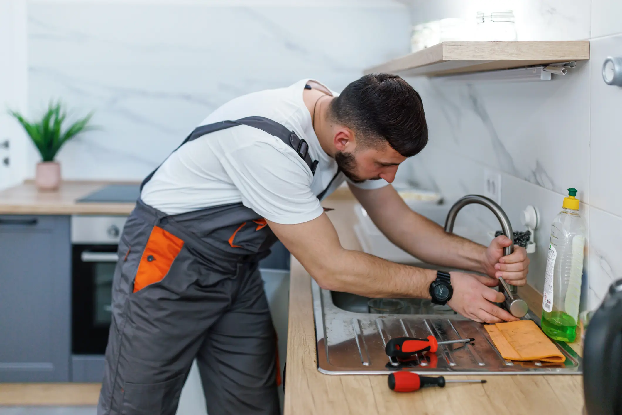 A plumber fixing a kitchen sink faucet with tools.