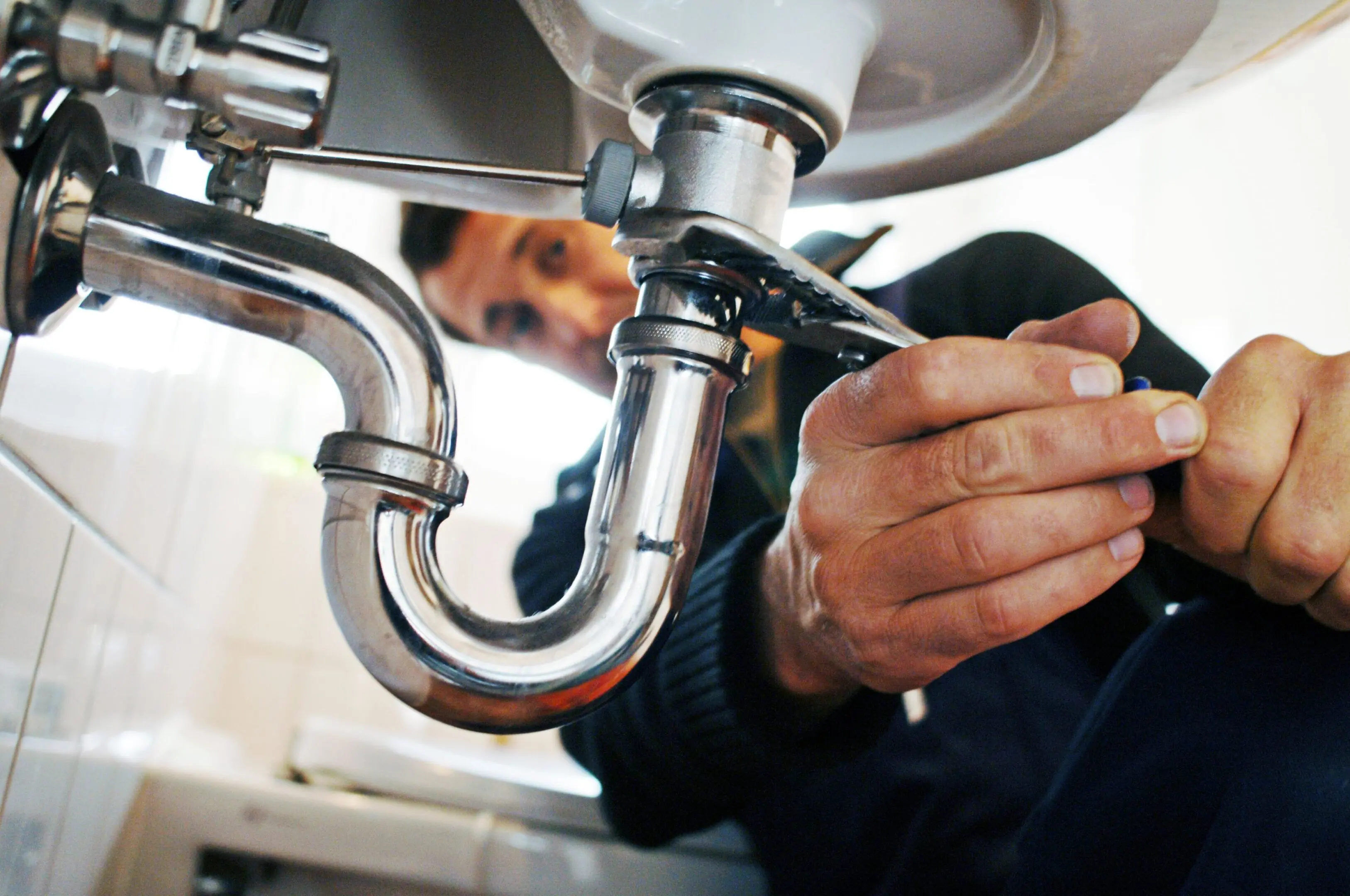 A plumber fixing a sink pipe underneath.