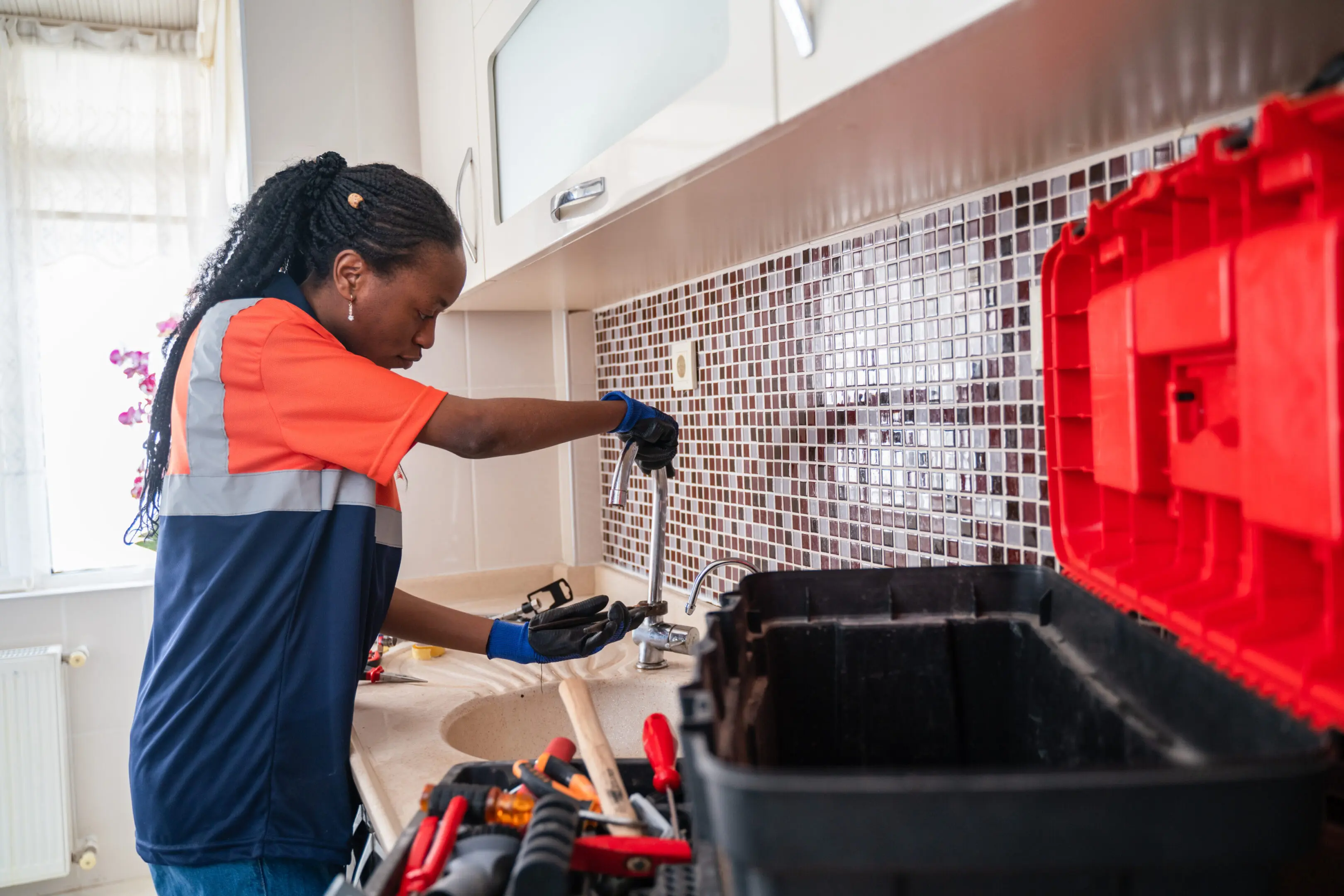 Technician fixing kitchen sink plumbing with tools.