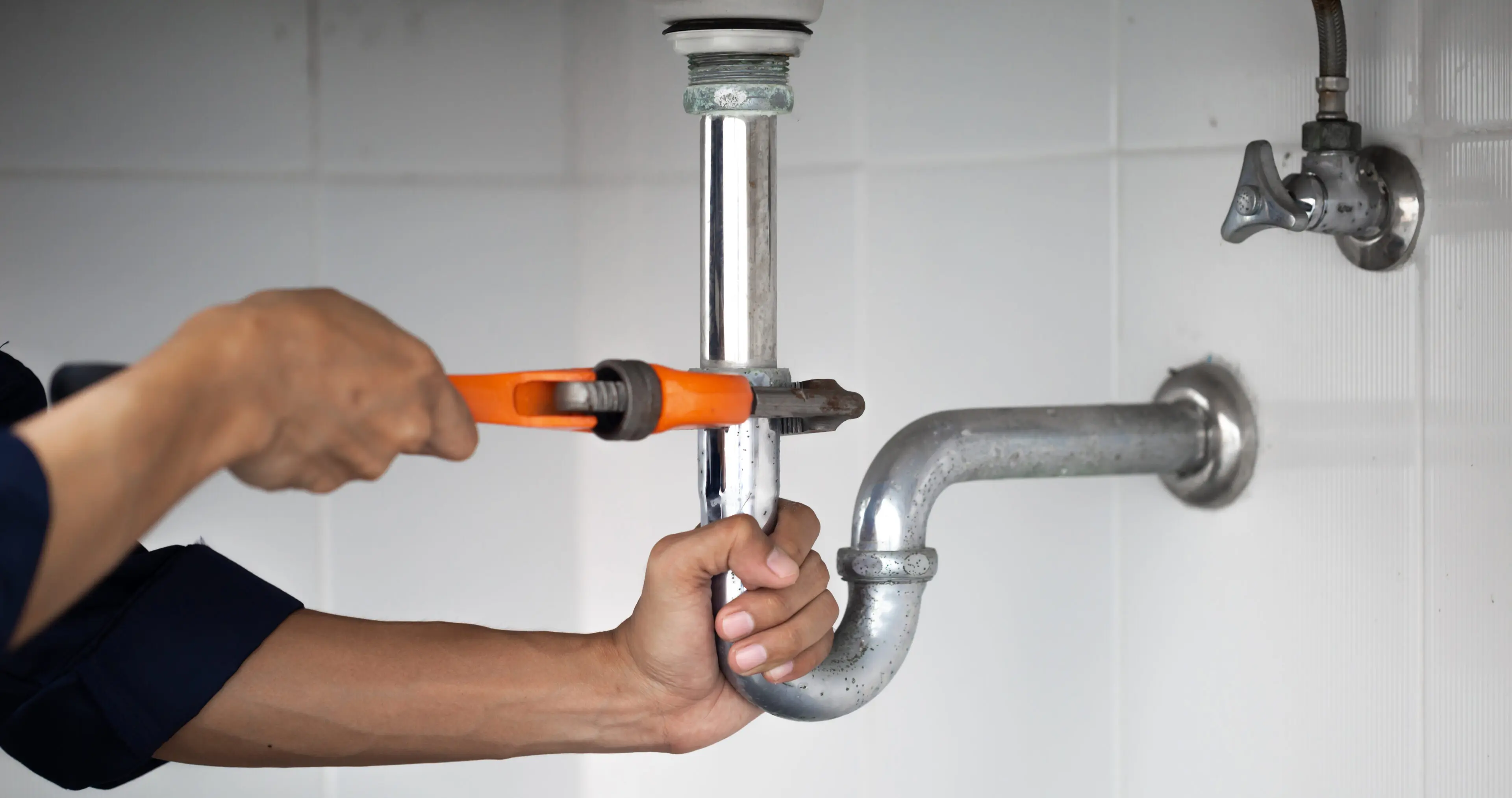 Person using a wrench to tighten plumbing under a sink.