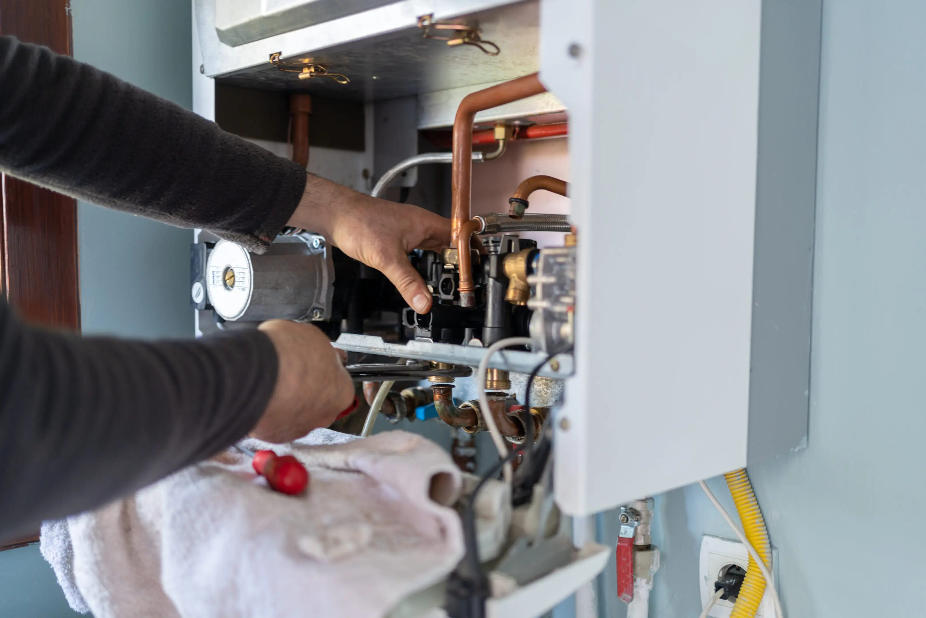 Technician repairing a home boiler system with various pipes and controls.