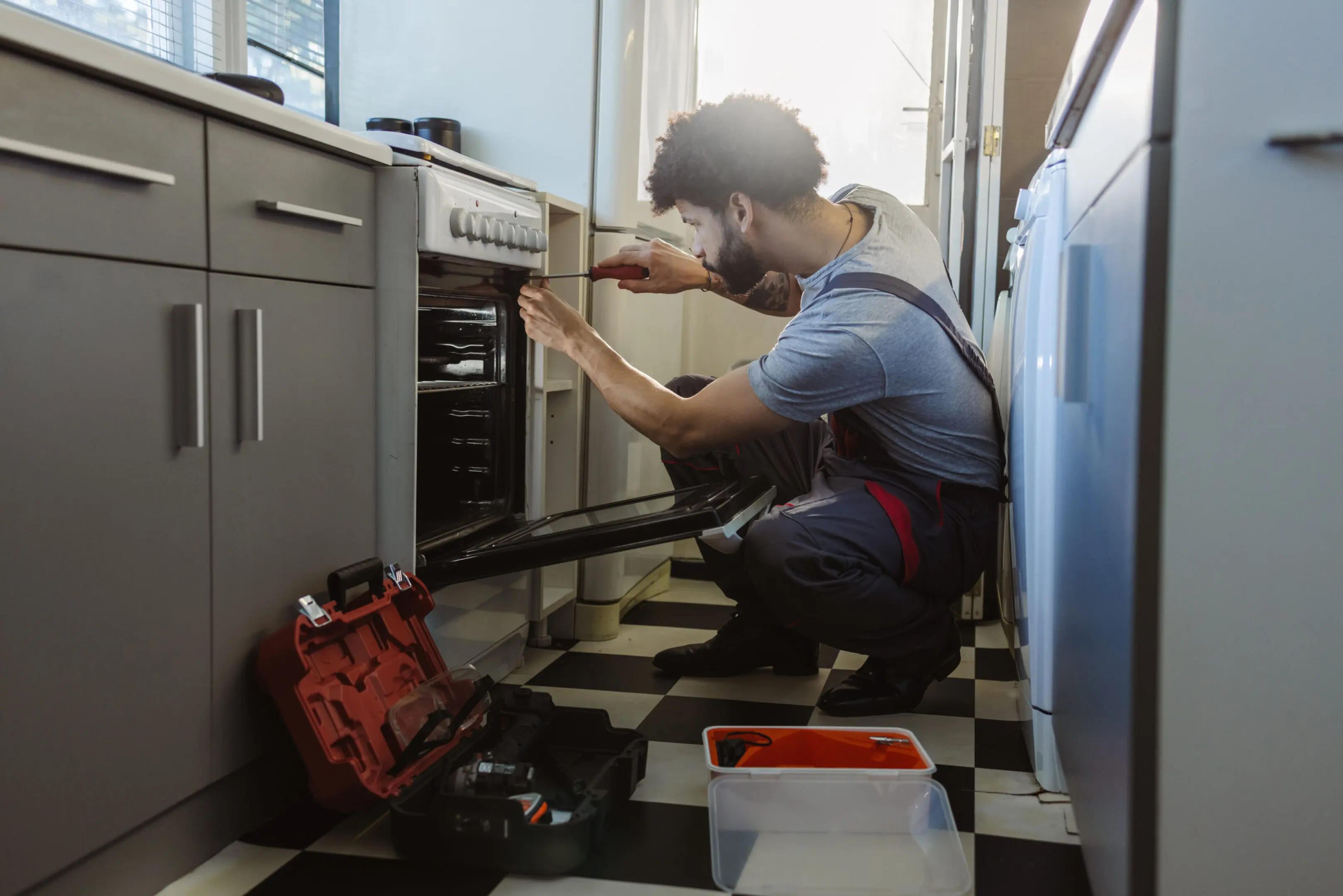 A technician repairing an oven in a kitchen with tools nearby.