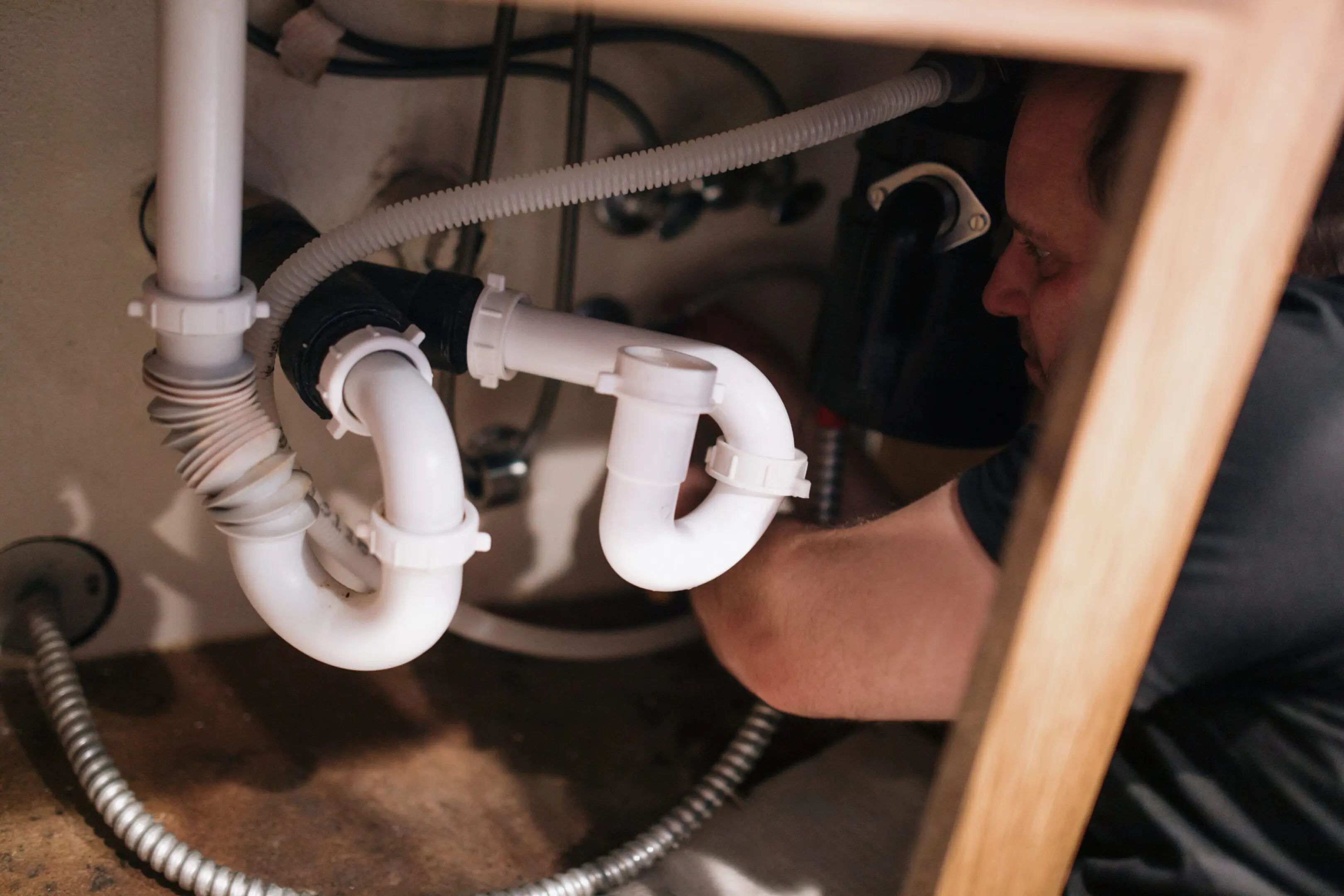A person repairing plumbing pipes under a sink.
