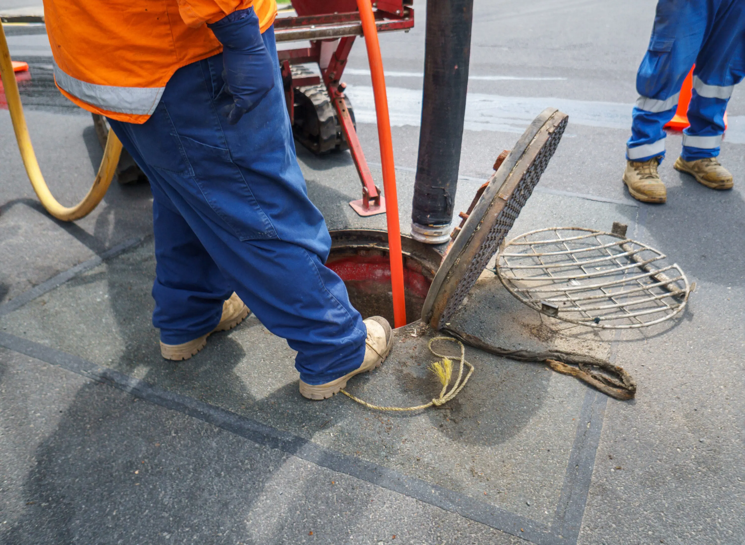 Worker using a tool to open a manhole cover on a street.