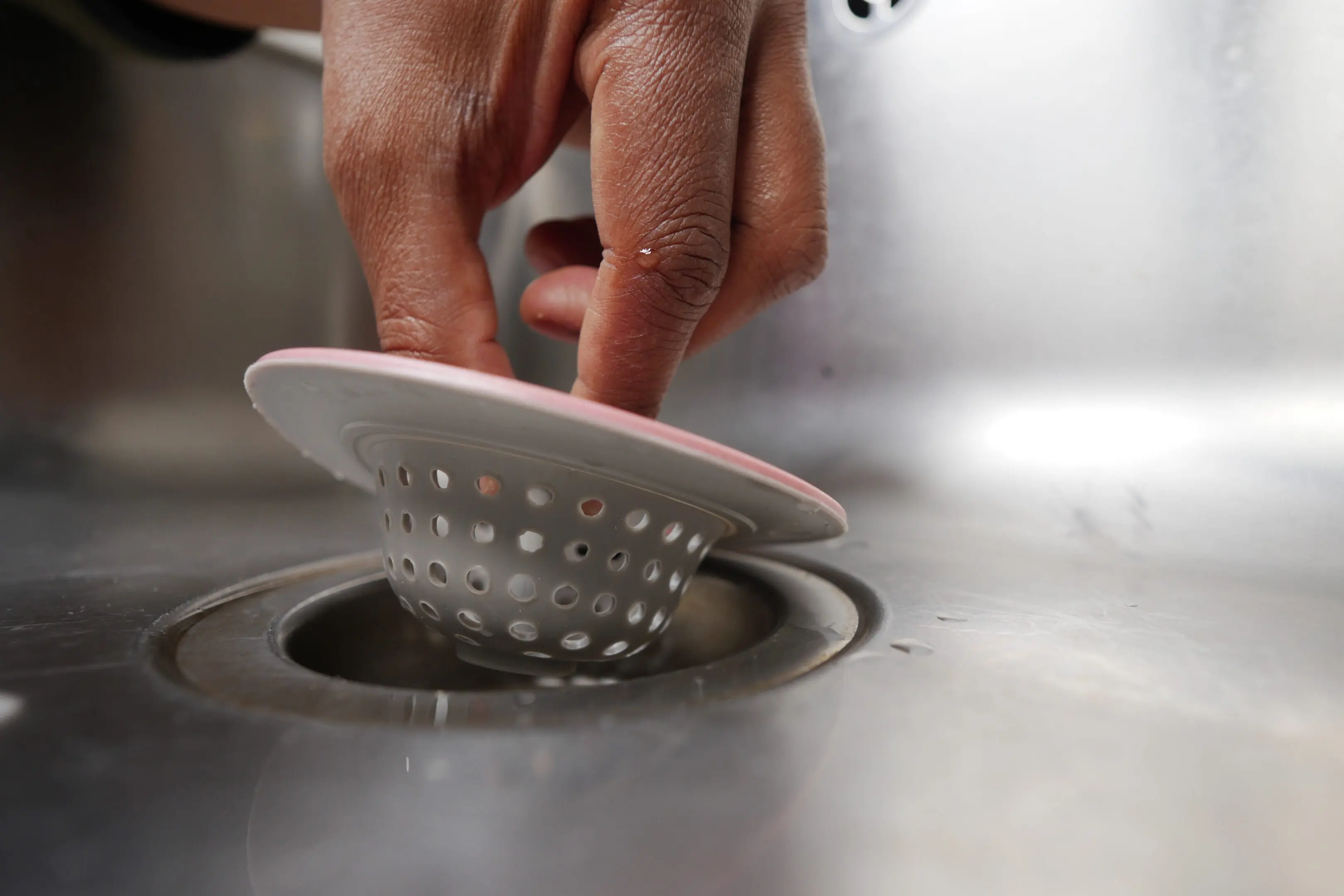 Hand removing a sink strainer from a kitchen drain.