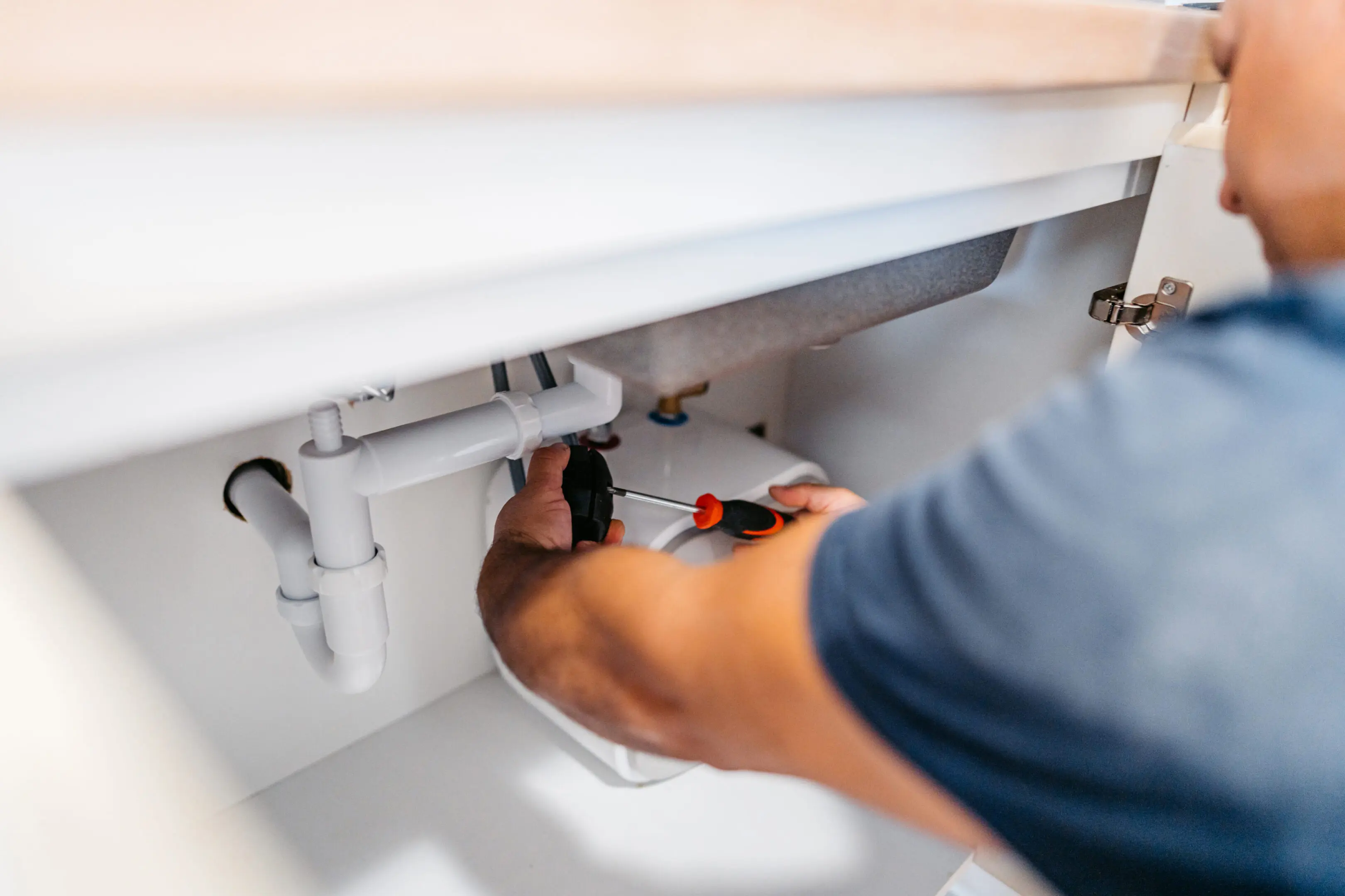 A person fixing plumbing under a sink with a wrench.