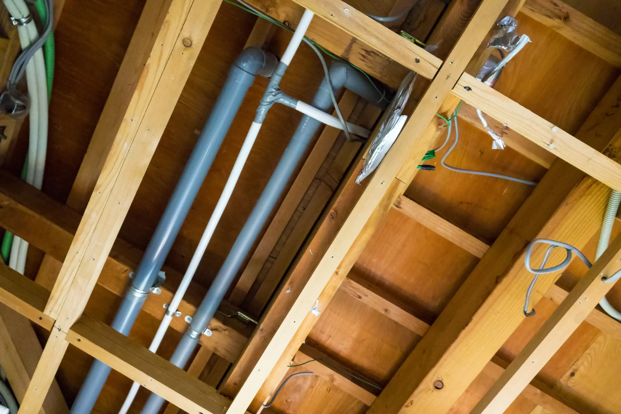Exposed plumbing pipes and electrical wiring in wooden ceiling framework.