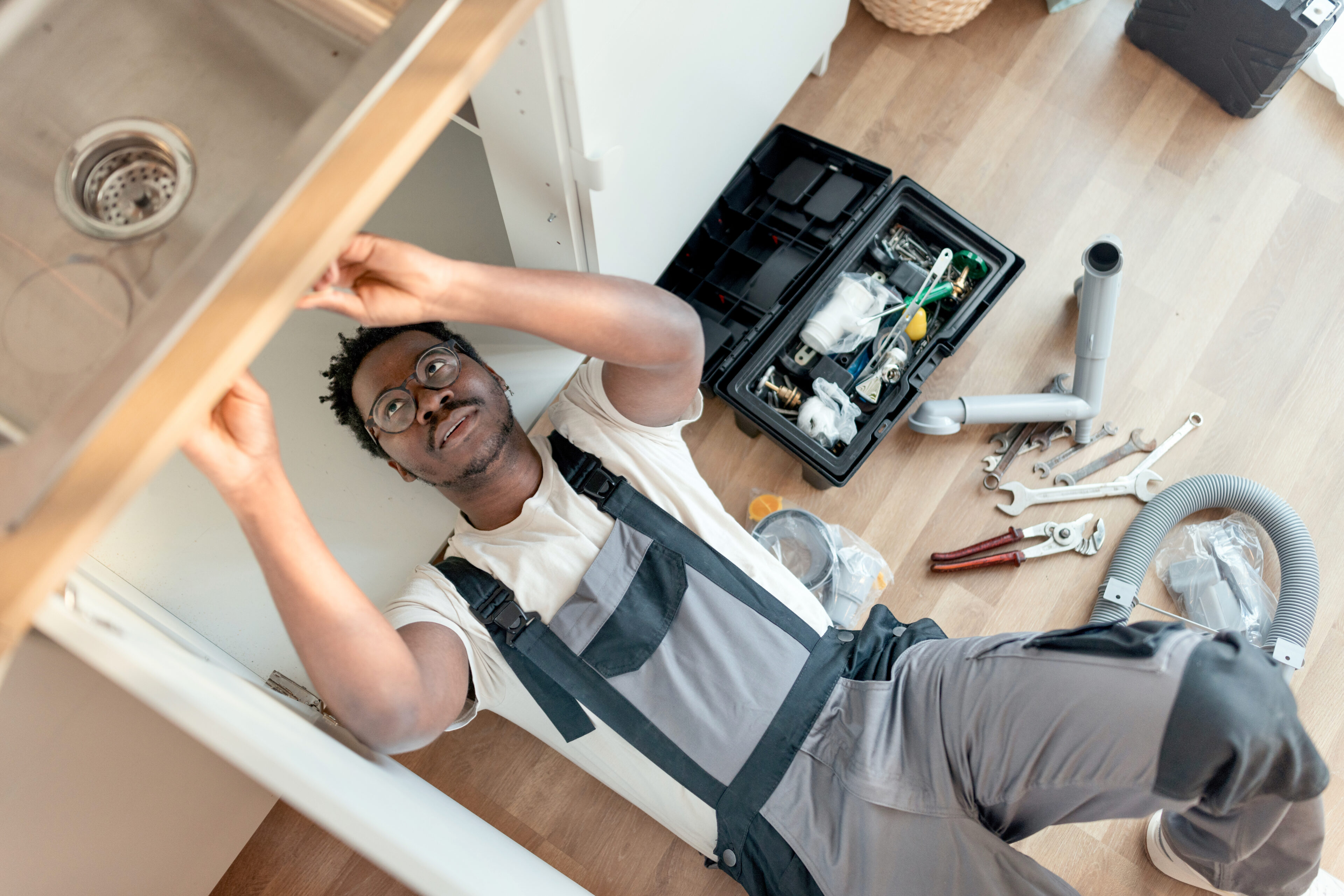 Handyman fixing plumbing under a kitchen sink.