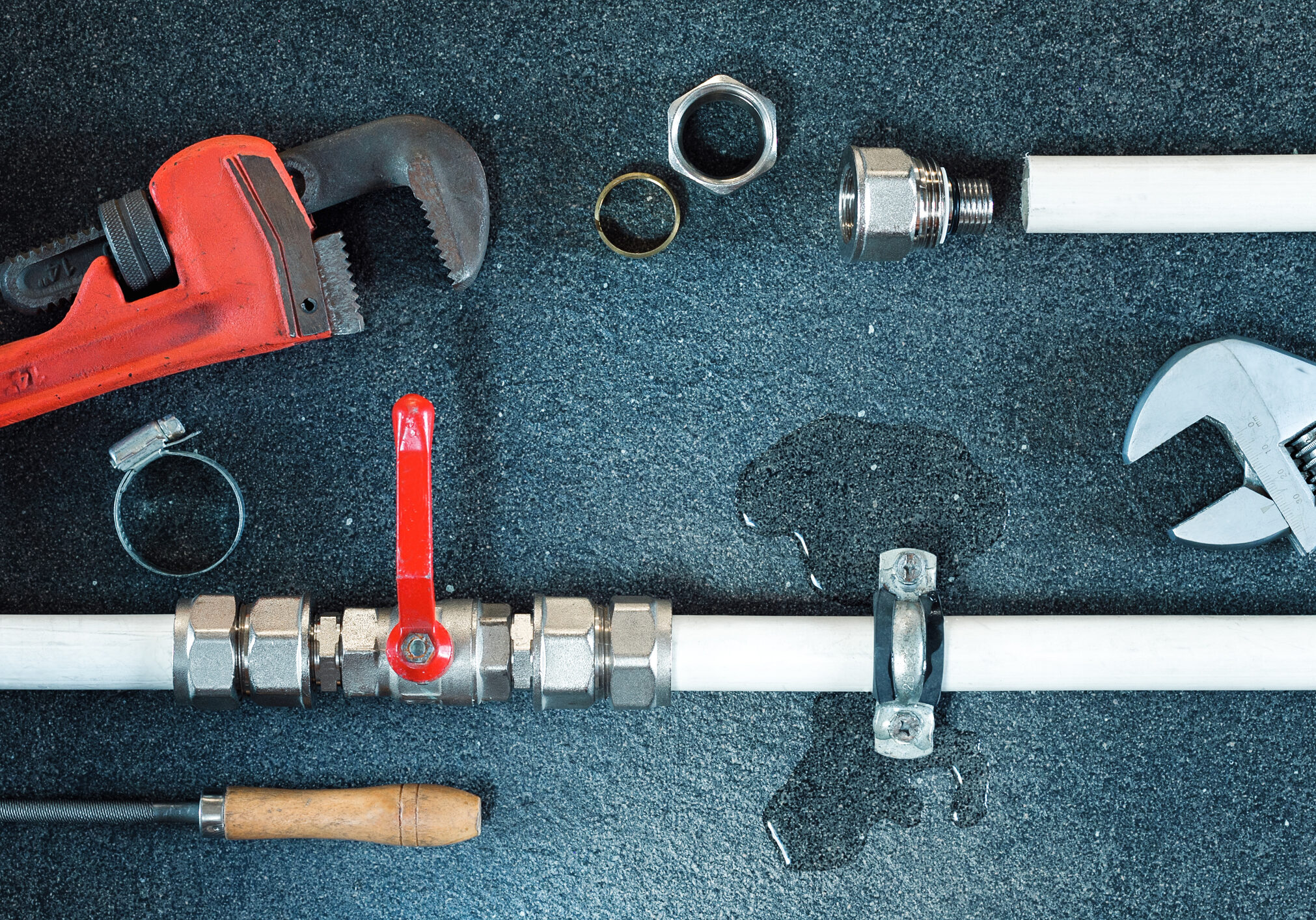 Plumbing tools and fittings arranged on a dark surface.