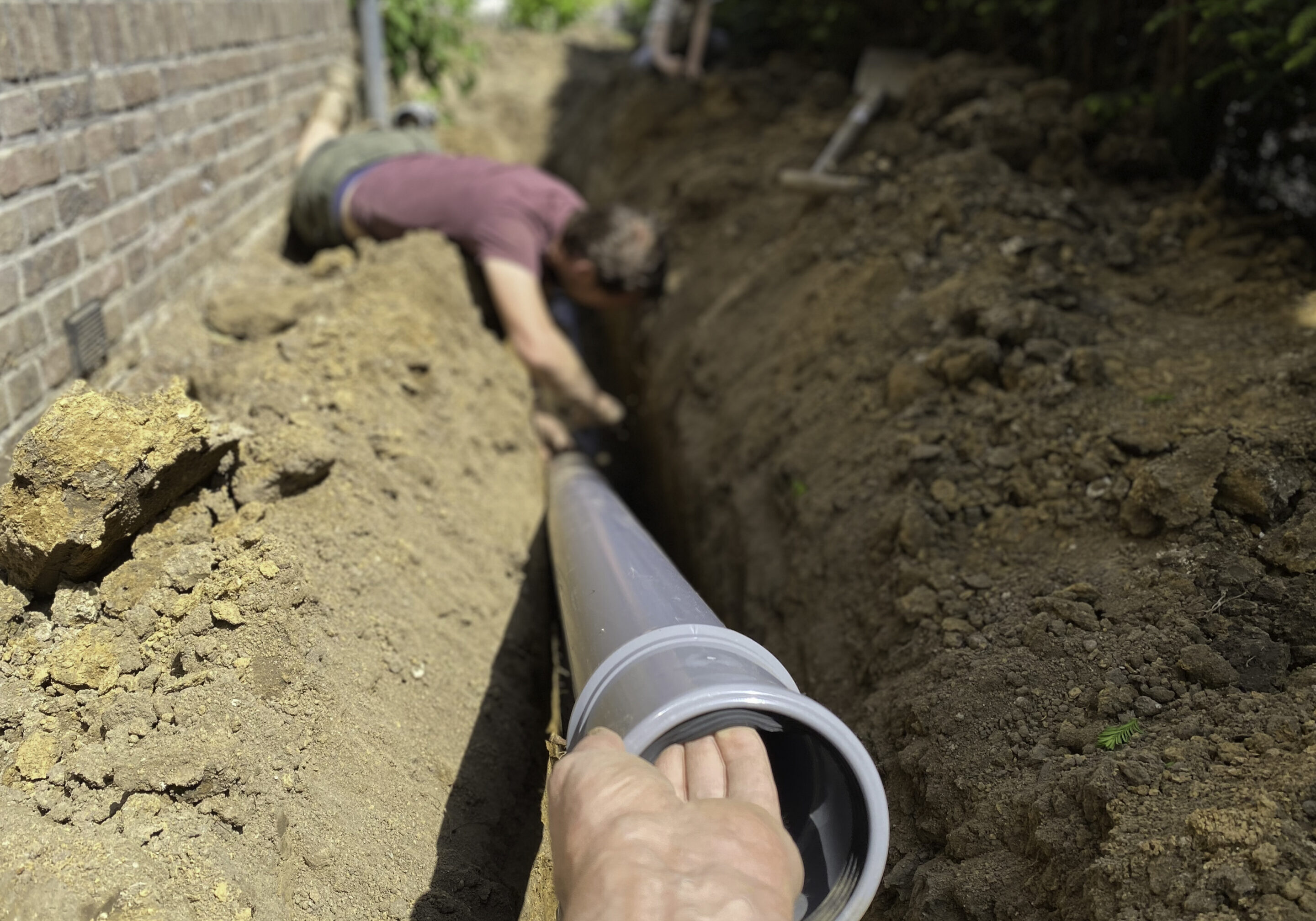Two people installing a large pipe in a trench outdoors.