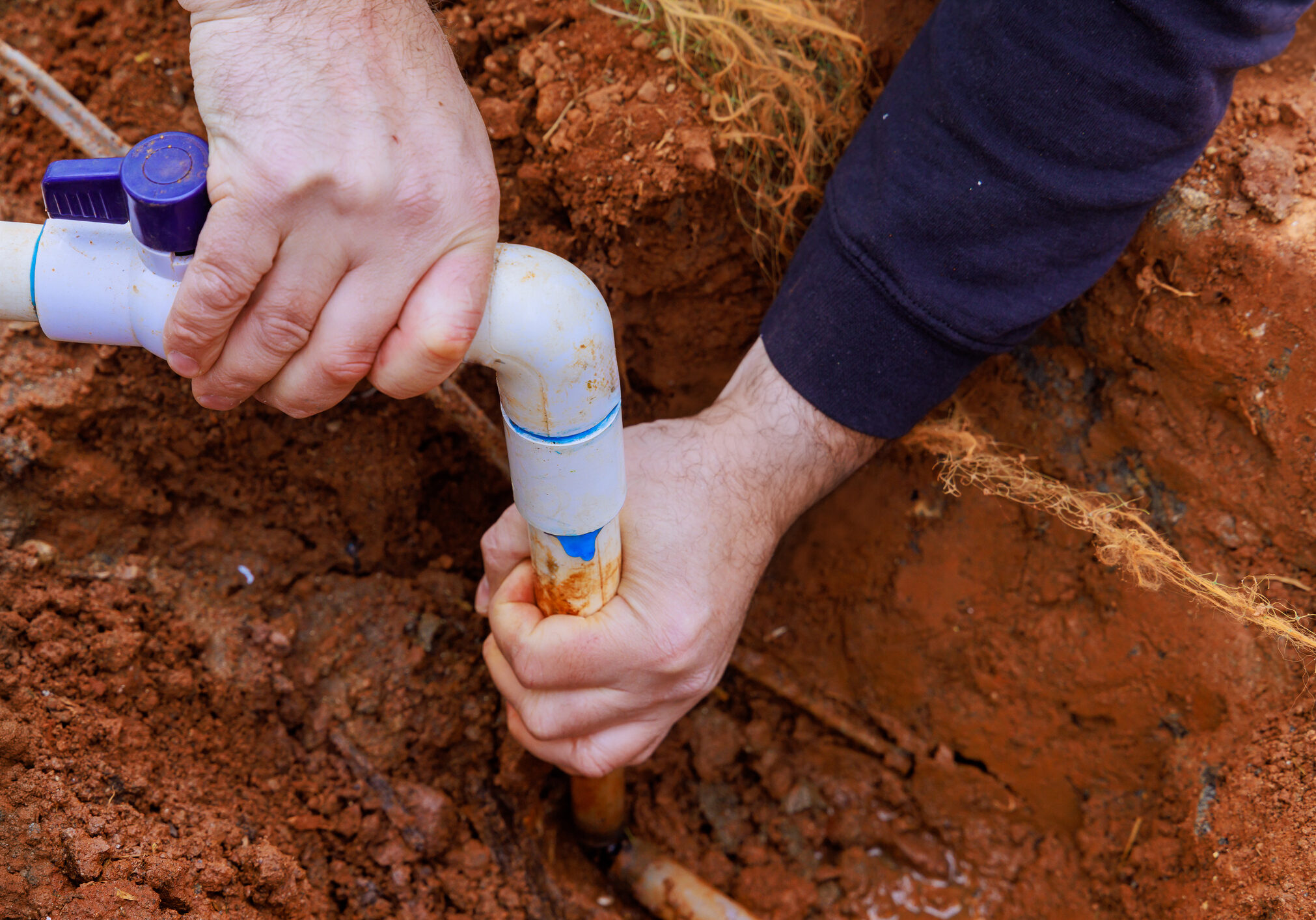 Hands fixing a pipe joint in the soil.