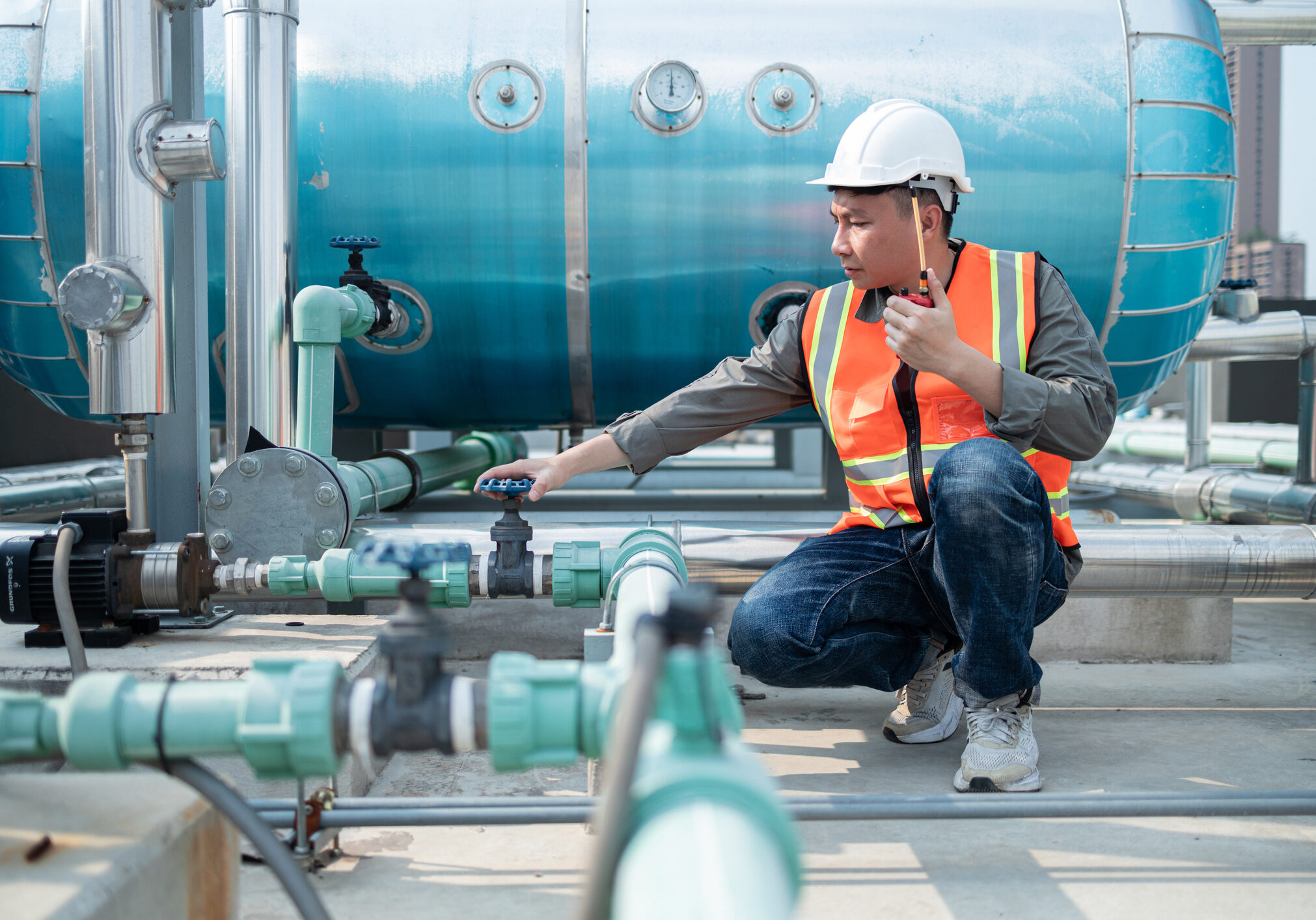 Engineer inspecting industrial pipelines while communicating via radio.
