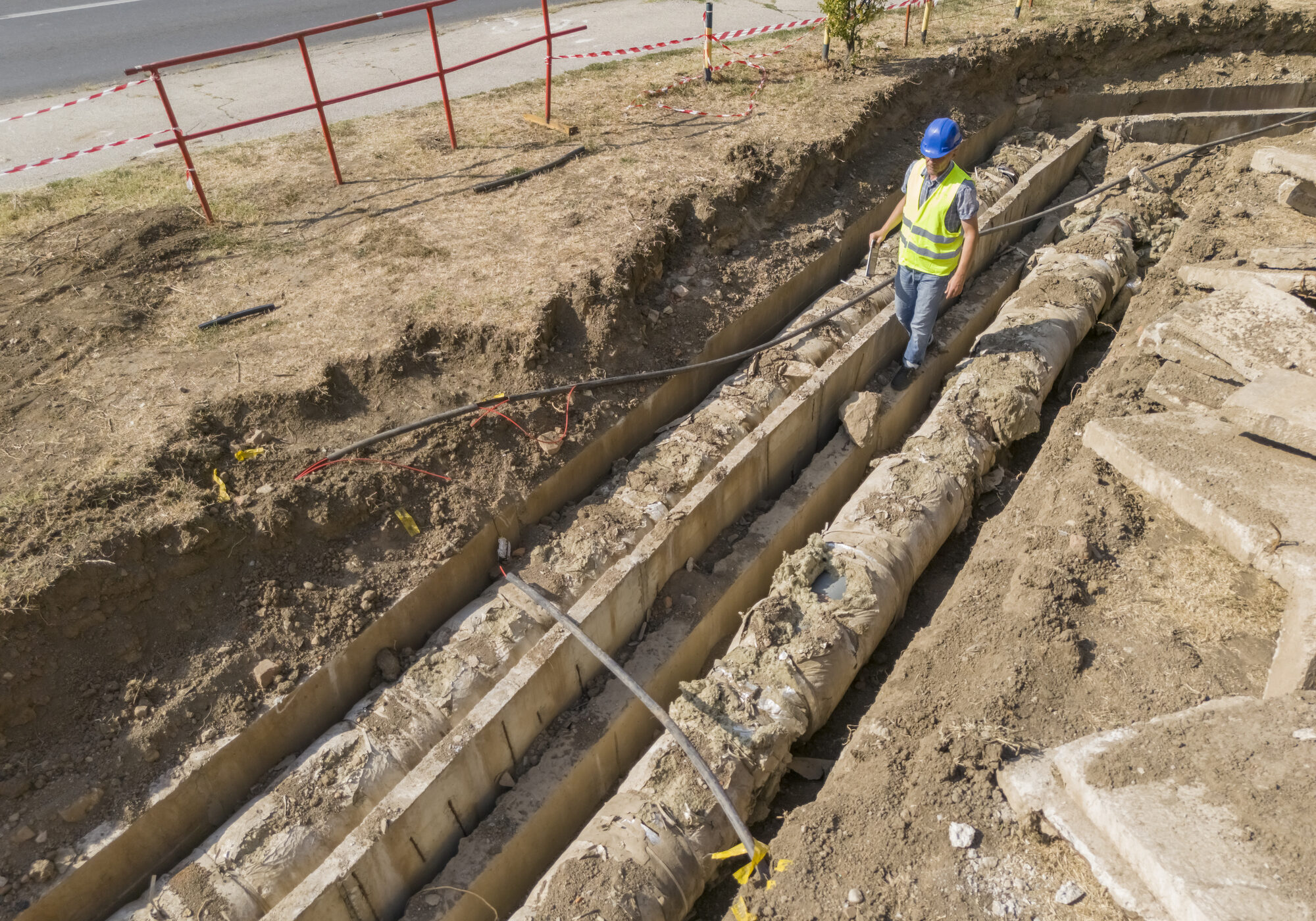 Construction worker inspecting large underground pipes in a trench.