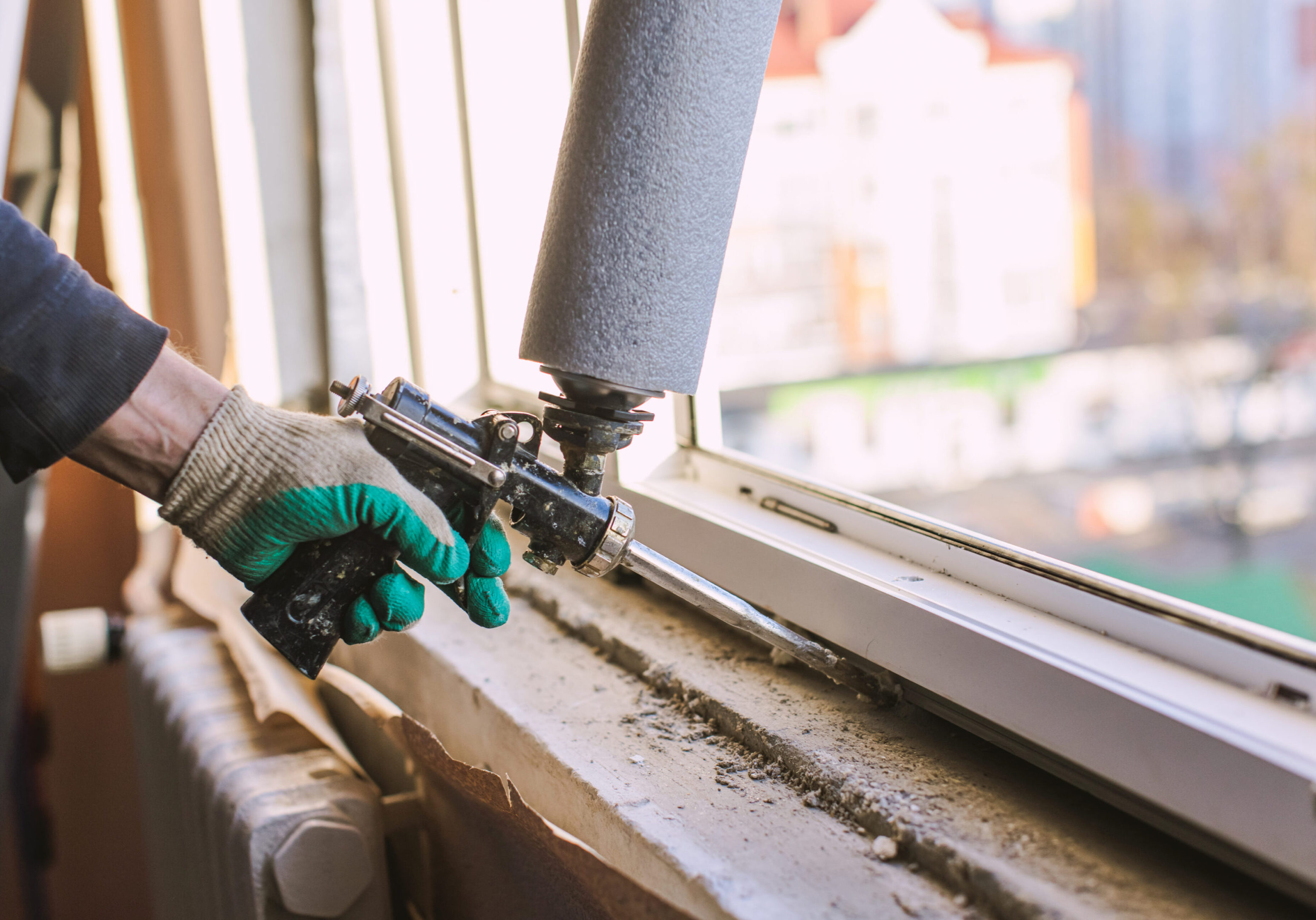 Worker applying foam insulation around a window frame.