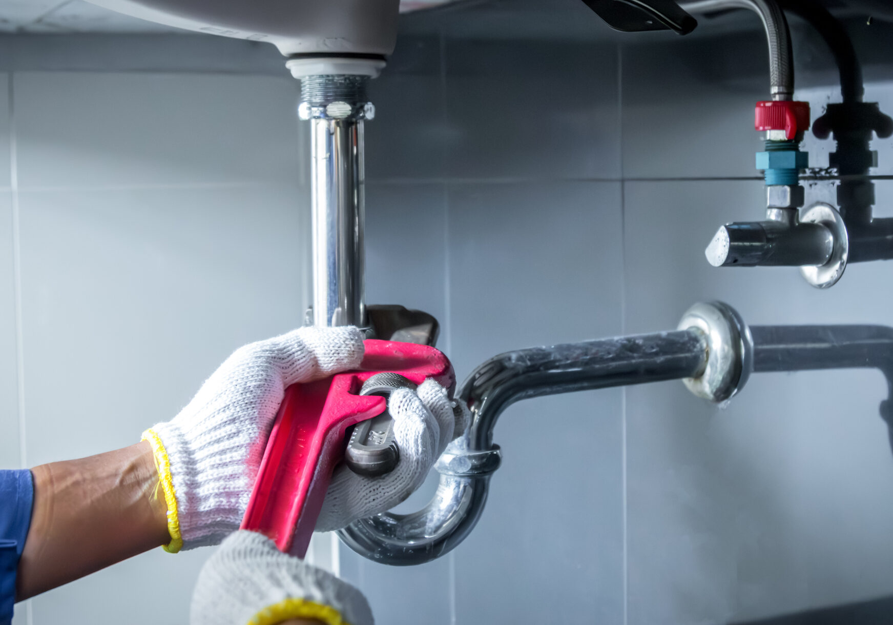 A plumber fixes a pipe under a sink using a wrench.
