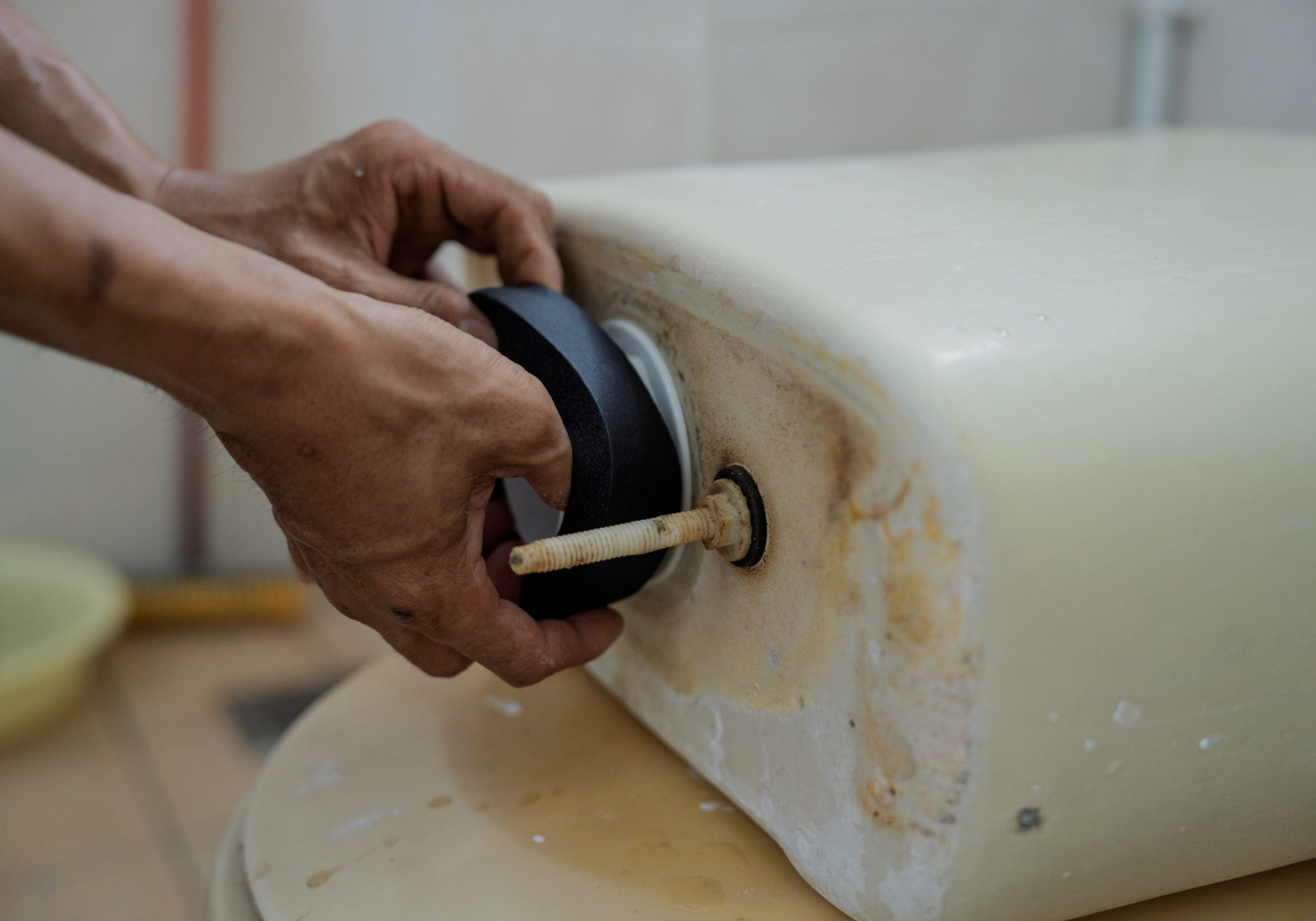 Hands fixing a toilet tank bolt with a rubber washer.