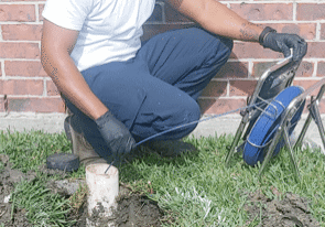 Man inspecting outdoor pipe near brick wall.